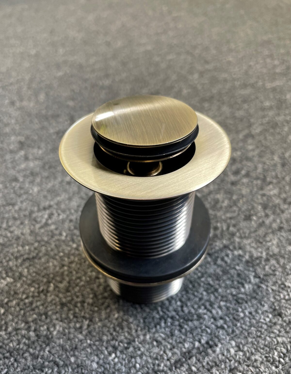 Bronze pop-up waste drain on textured surface.