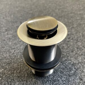 Bronze pop-up waste drain on textured surface.