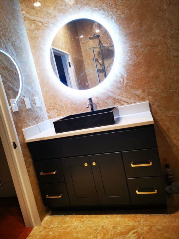 Modern bathroom vanity with illuminated round mirror and marble walls.