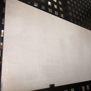 Large gray tile displayed on a black perforated metal stand.