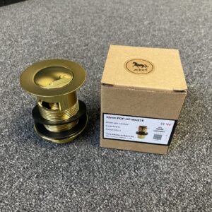 Gold pop-up waste with overflow next to labeled box on carpet.