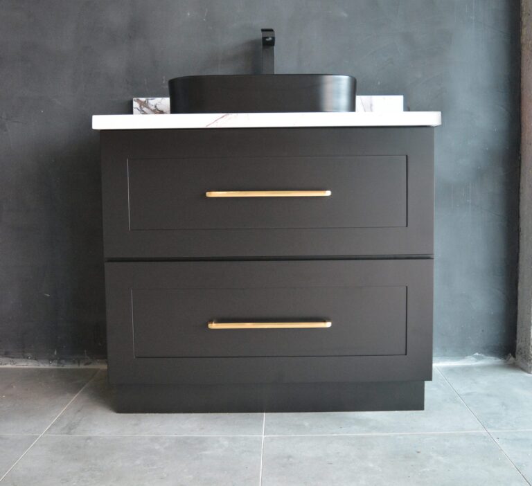 Black freestanding vanity with gold handles against dark wall.
