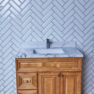 Wooden bathroom vanity with marble countertop and herringbone tile backsplash.
