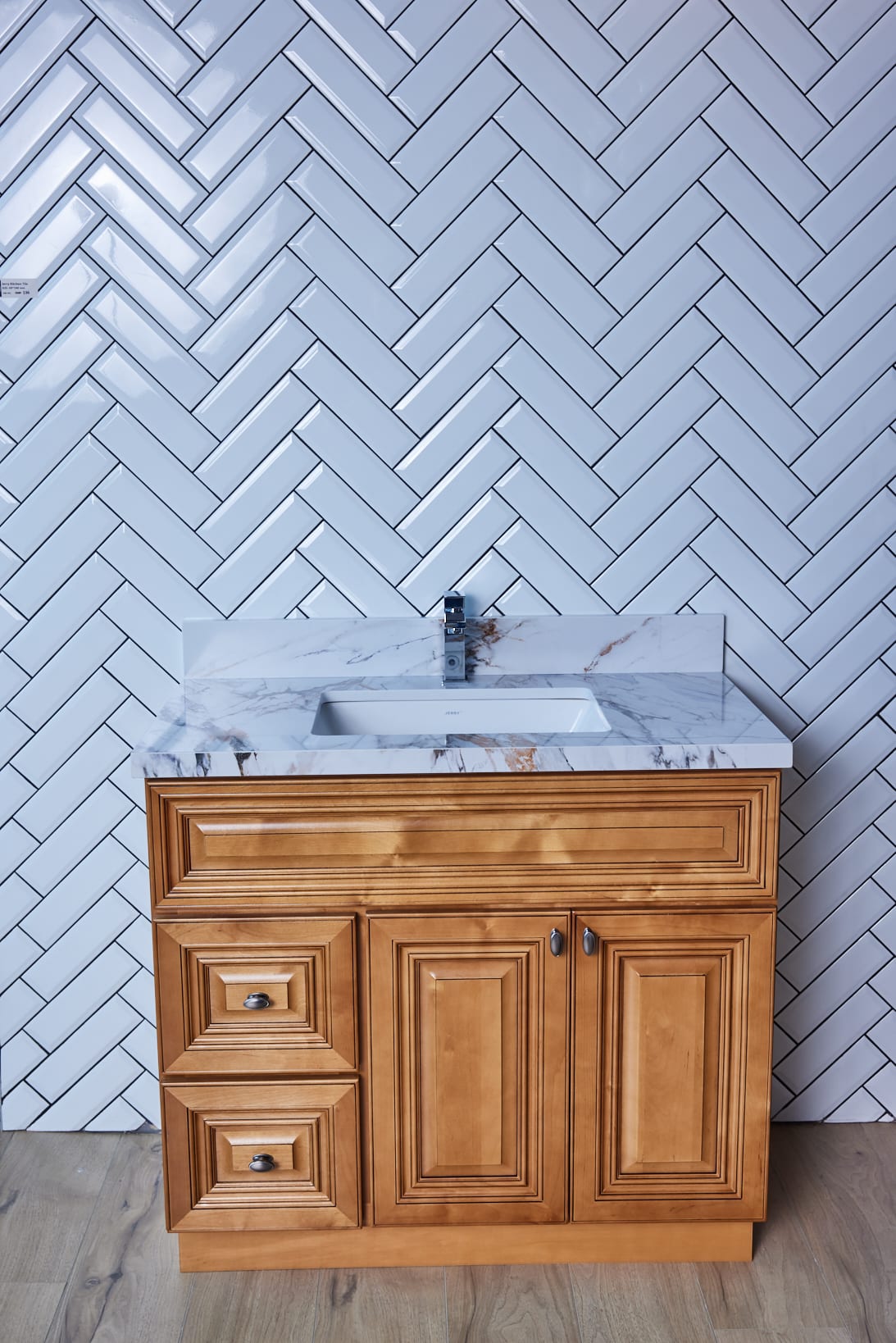 Wooden bathroom vanity with marble countertop and herringbone tile backsplash.