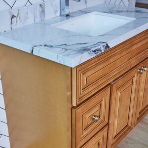 Wooden bathroom vanity with marble countertop and herringbone tile backsplash.