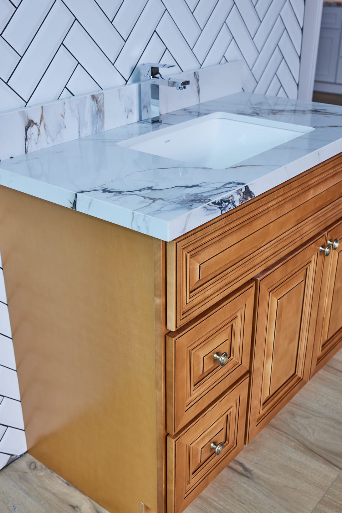 Wooden bathroom vanity with marble countertop and herringbone tile backsplash.