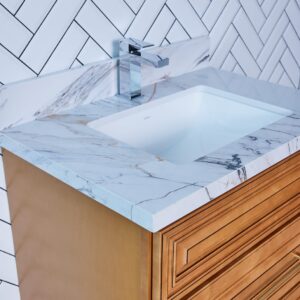 Marble countertop with sink and wooden cabinet against herringbone tile wall.