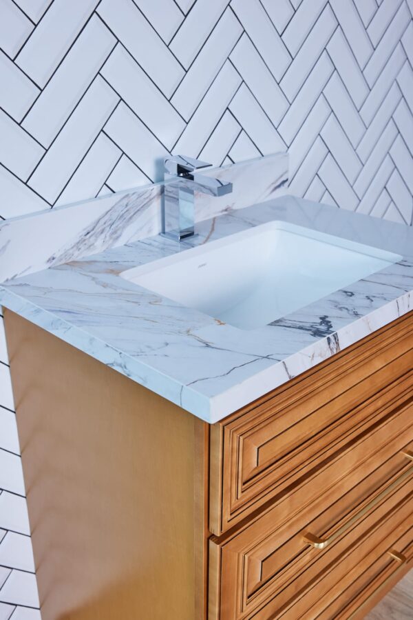 Marble countertop with sink and wooden cabinet against herringbone tile wall.