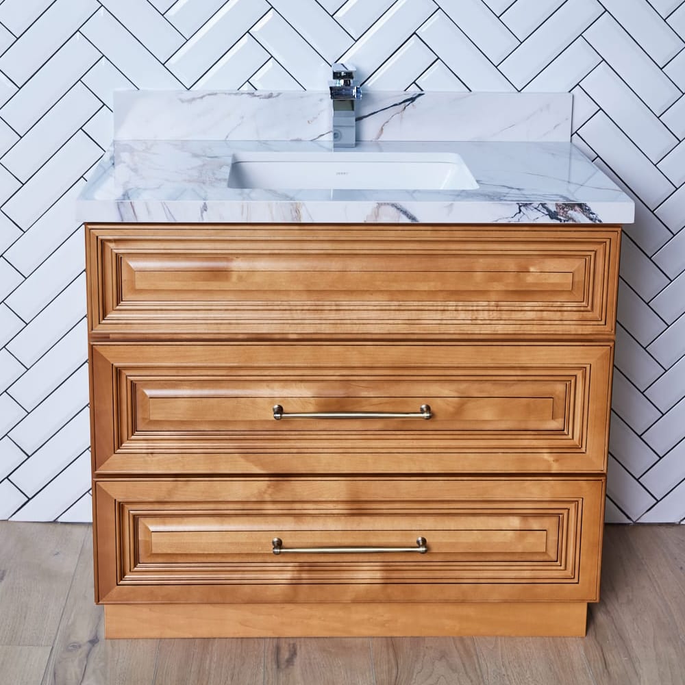 Wooden bathroom vanity with marble countertop and herringbone tile backsplash.