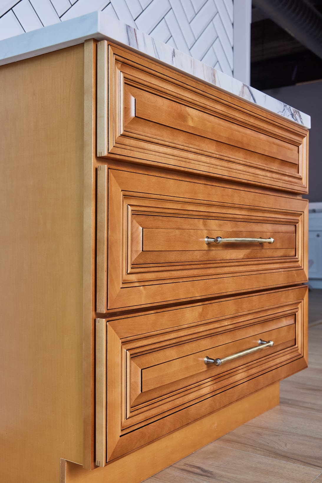 Wooden kitchen cabinet with three drawers and metal handles.