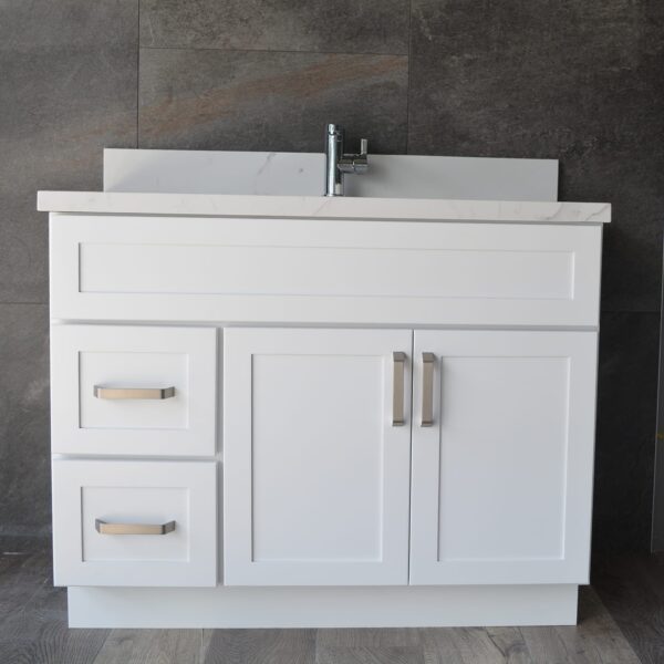 DSC_0194.jpg White bathroom vanity with drawers and sink against dark tiled wall.
