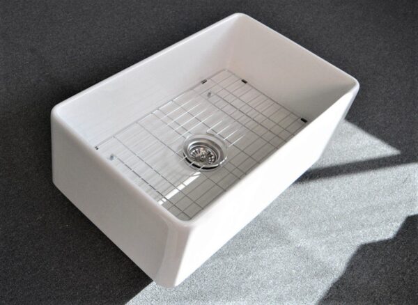 White kitchen sink with metal grid on dark countertop.