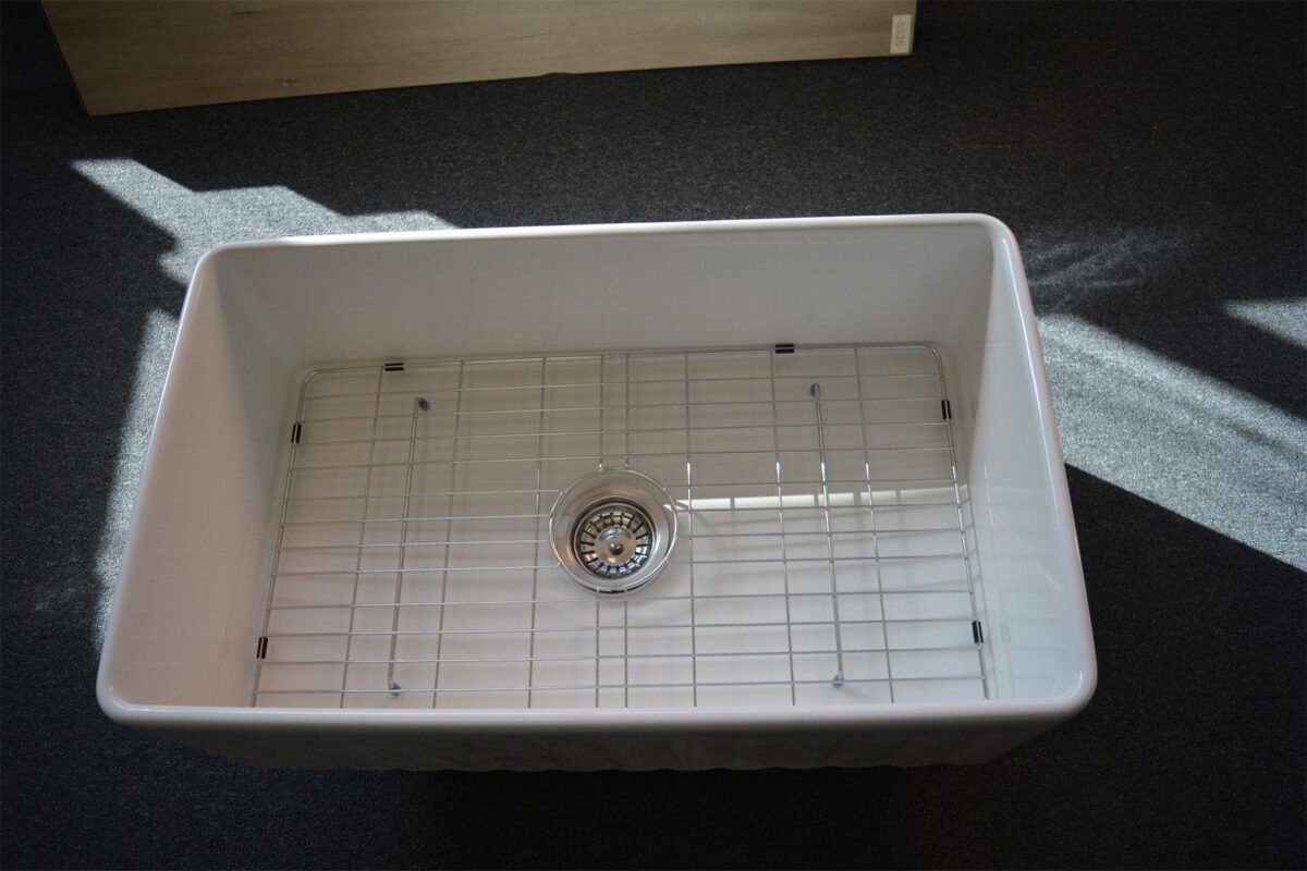 White kitchen sink with metal grid and drain.