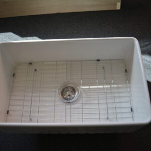 White kitchen sink with metal grid and drain.