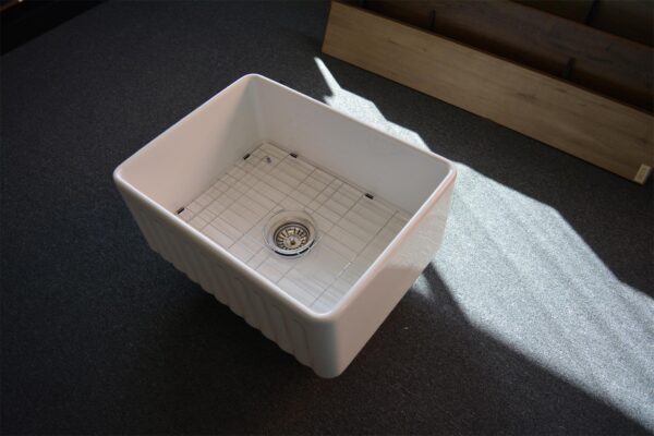 A white ceramic kitchen sink on a dark carpeted floor.