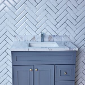 Blue bathroom vanity with marble countertop and herringbone tile backsplash.
