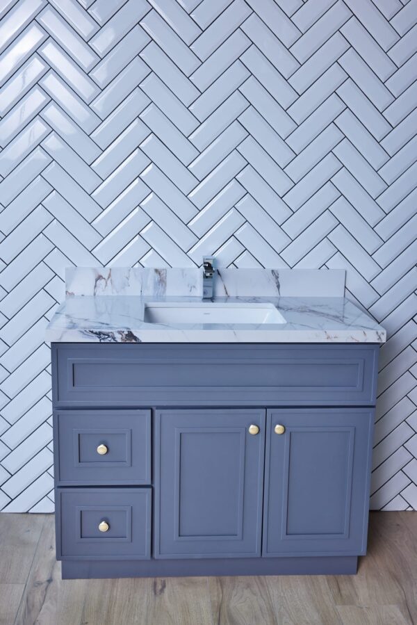 Blue bathroom vanity with marble countertop and herringbone tile backsplash.