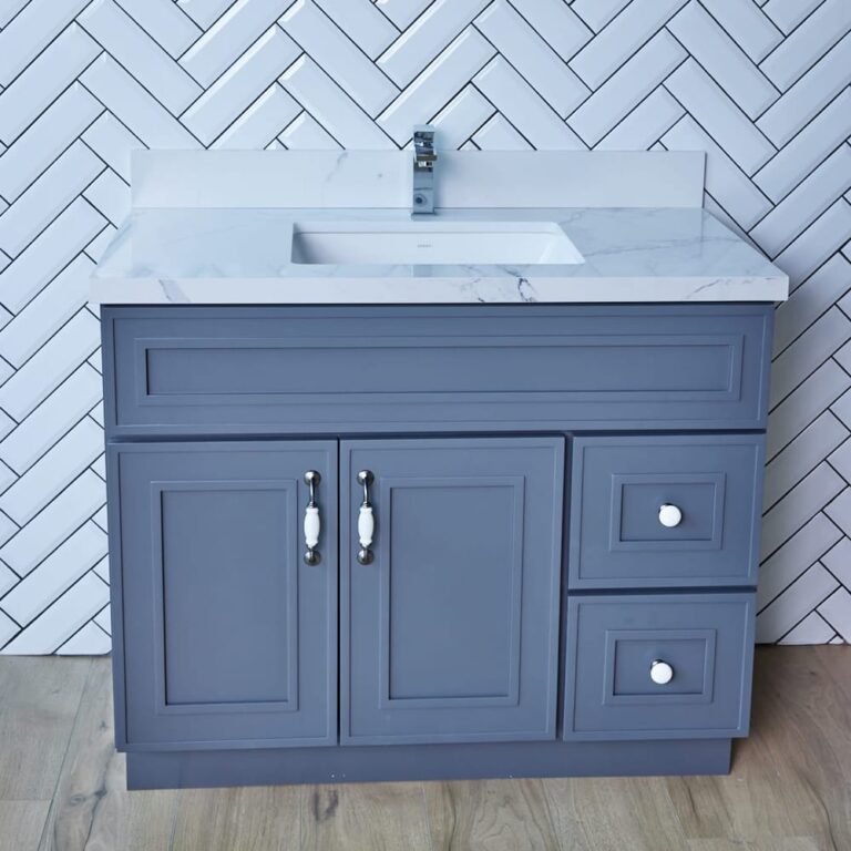 Gray bathroom vanity with marble countertop and herringbone tile backsplash.