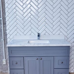 Gray bathroom vanity with marble countertop and herringbone tile backsplash.