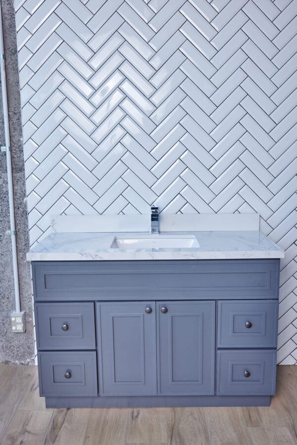 Gray bathroom vanity with marble countertop and herringbone tile backsplash.