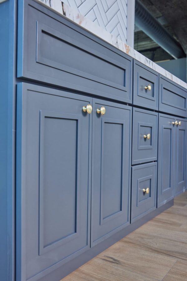 Blue kitchen cabinets with gold handles and marble countertop.