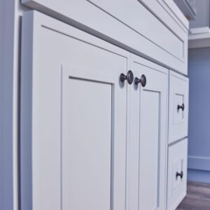 White kitchen cabinets with black knobs on a wooden floor.