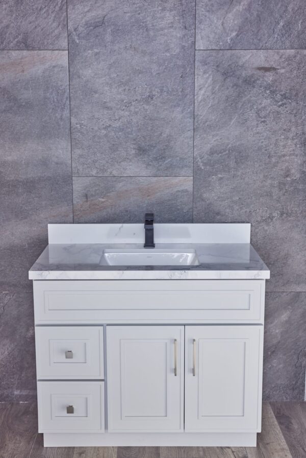 White bathroom vanity with marble countertop against gray stone wall.