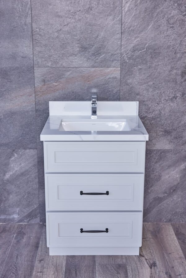 White bathroom vanity with three drawers and a sink, against a gray tiled wall.