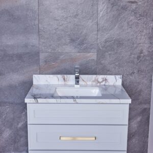 White bathroom vanity with marble countertop and gold handles against gray tile wall.