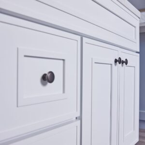White kitchen cabinets with black knobs and a marble countertop.