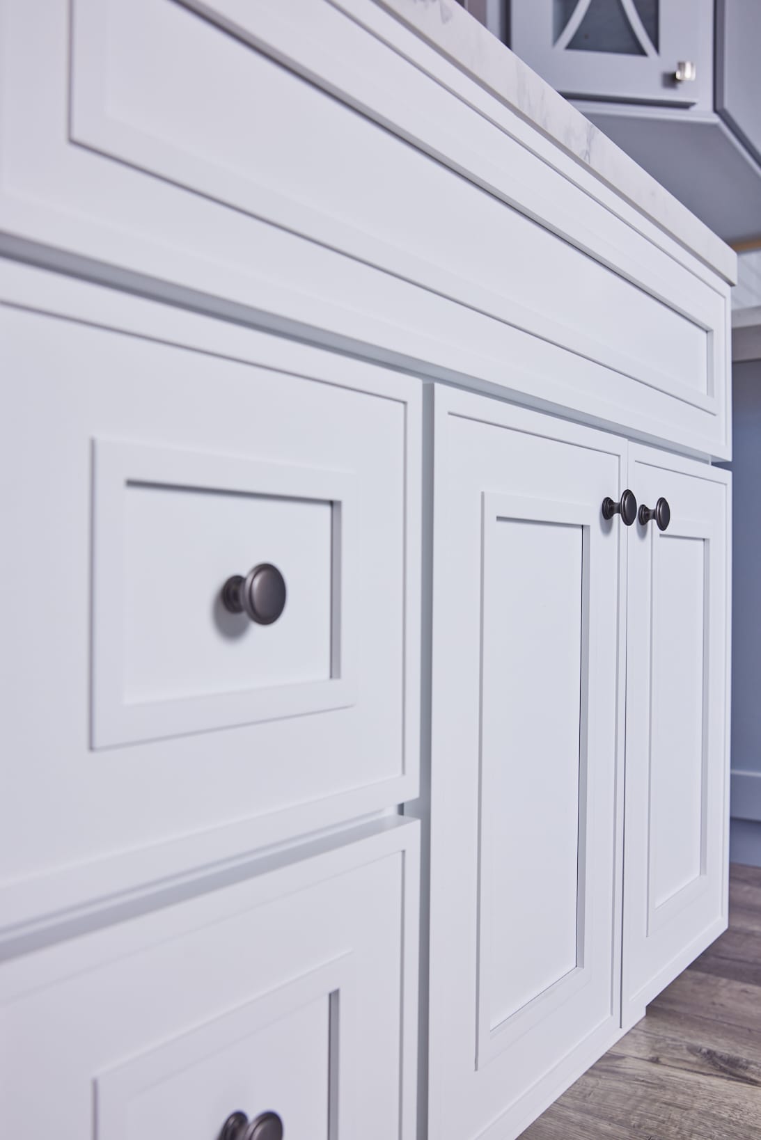 White kitchen cabinets with black knobs and a marble countertop.