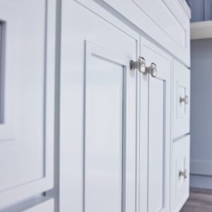 White kitchen cabinets with silver handles on a wooden floor.
