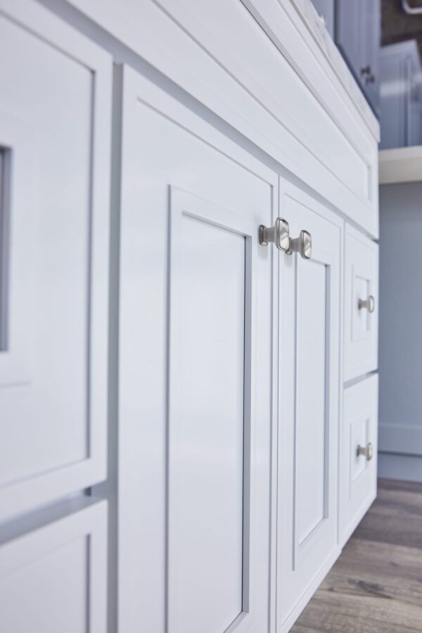 White kitchen cabinets with silver handles on a wooden floor.