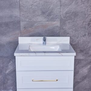 White bathroom vanity with marble countertop and gold handles against gray tile wall.