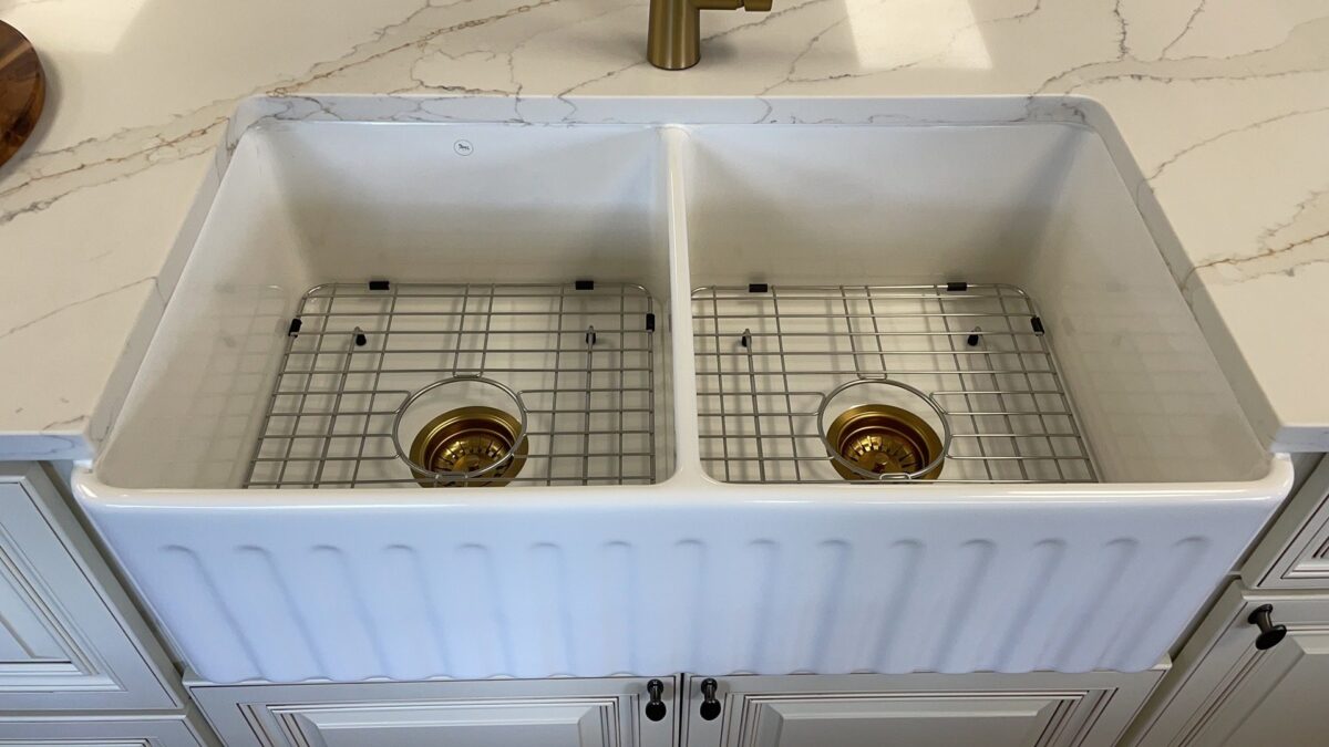 Double farmhouse sink with gold drain covers on marble countertop.