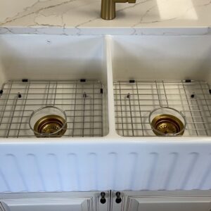 Double farmhouse sink with gold drain covers on marble countertop.