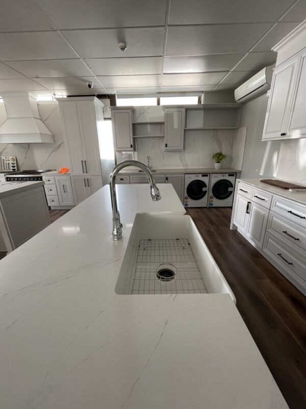 Modern kitchen with white cabinetry, island sink, and laundry appliances.