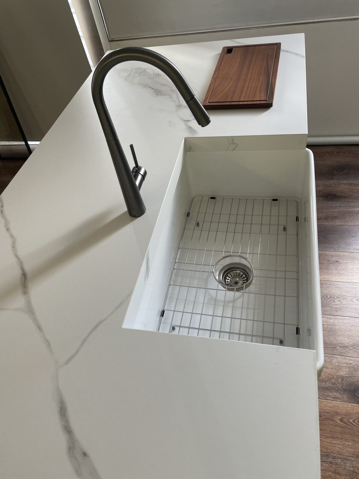 Modern kitchen sink with marble countertop and wooden cutting board.