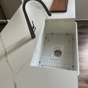 Modern kitchen sink with marble countertop and wooden cutting board.