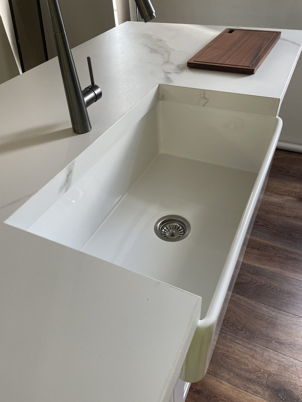 Modern kitchen sink with marble countertop and wooden cutting board.