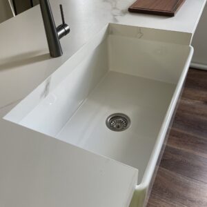 Modern kitchen sink with marble countertop and wooden cutting board.