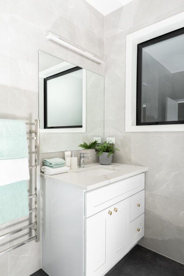Modern bathroom vanity with white cabinet, mirror, and potted plants.