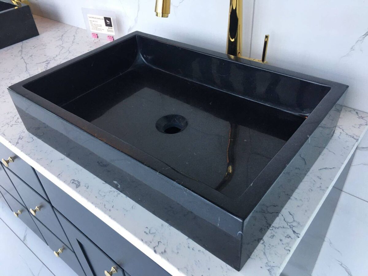 Black rectangular sink on marble countertop with gold faucet.
