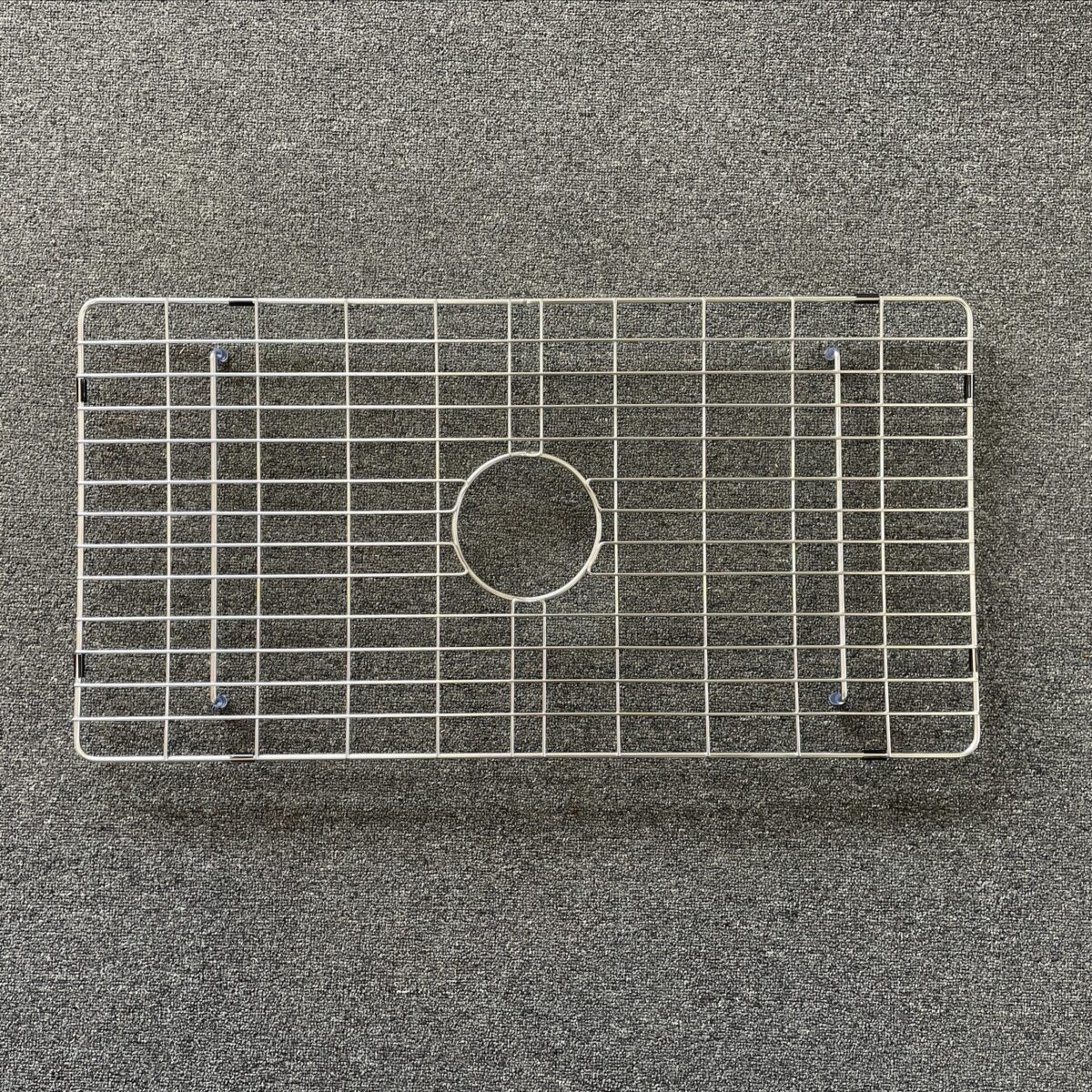 Stainless steel sink grid on a textured surface.