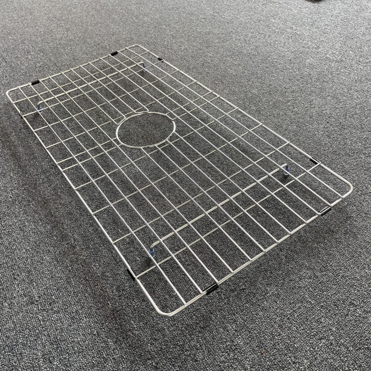 Stainless steel sink grid on gray carpet.