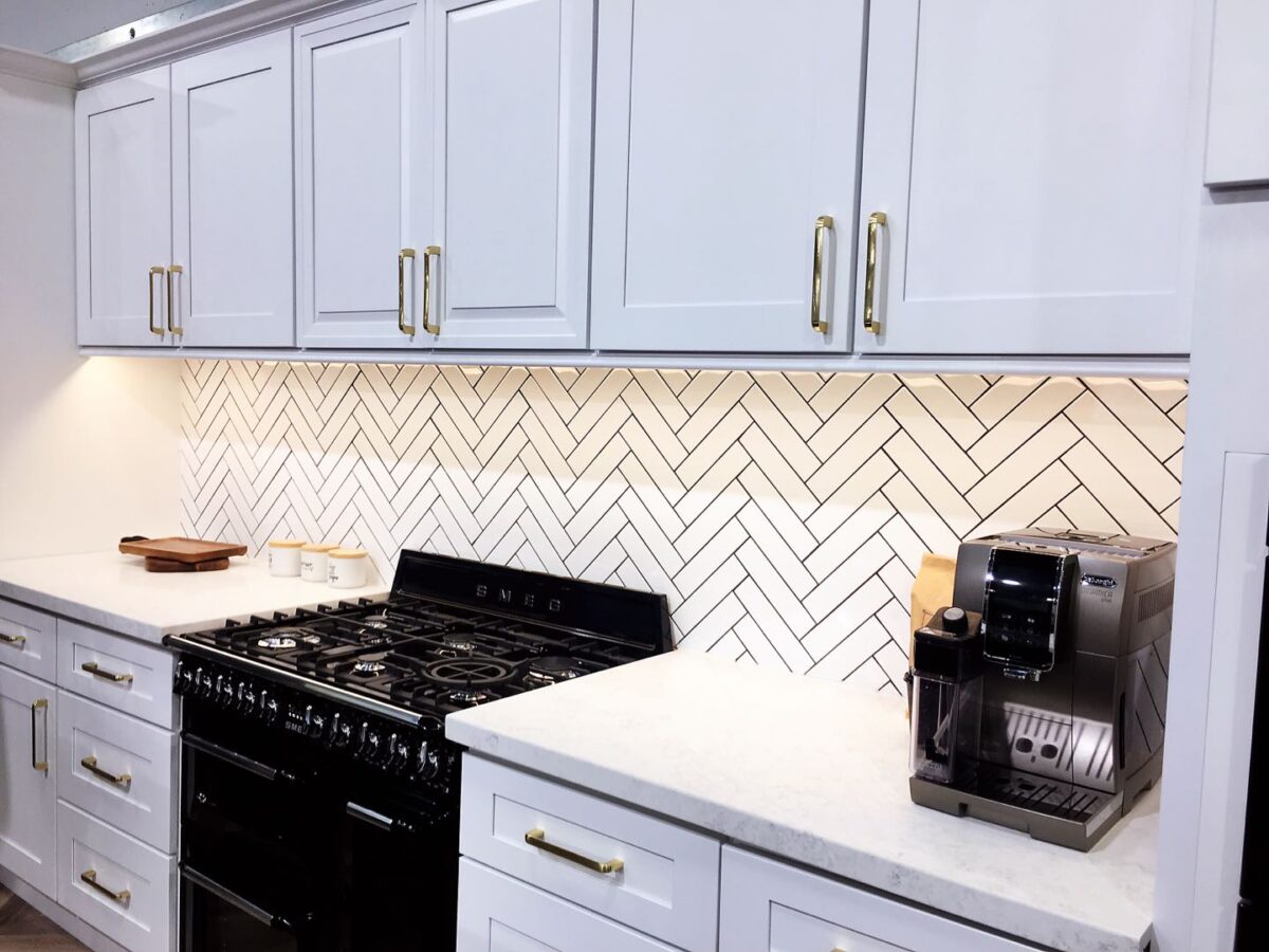 Modern kitchen with white cabinets, herringbone backsplash, and espresso machine.