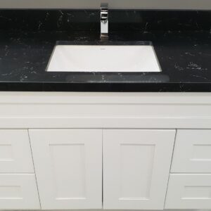 White bathroom vanity with black countertop and sink.
