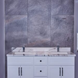 White bathroom vanity with marble countertop against gray stone wall.