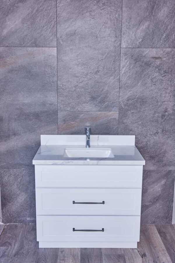 White bathroom vanity with sink against gray tiled wall.