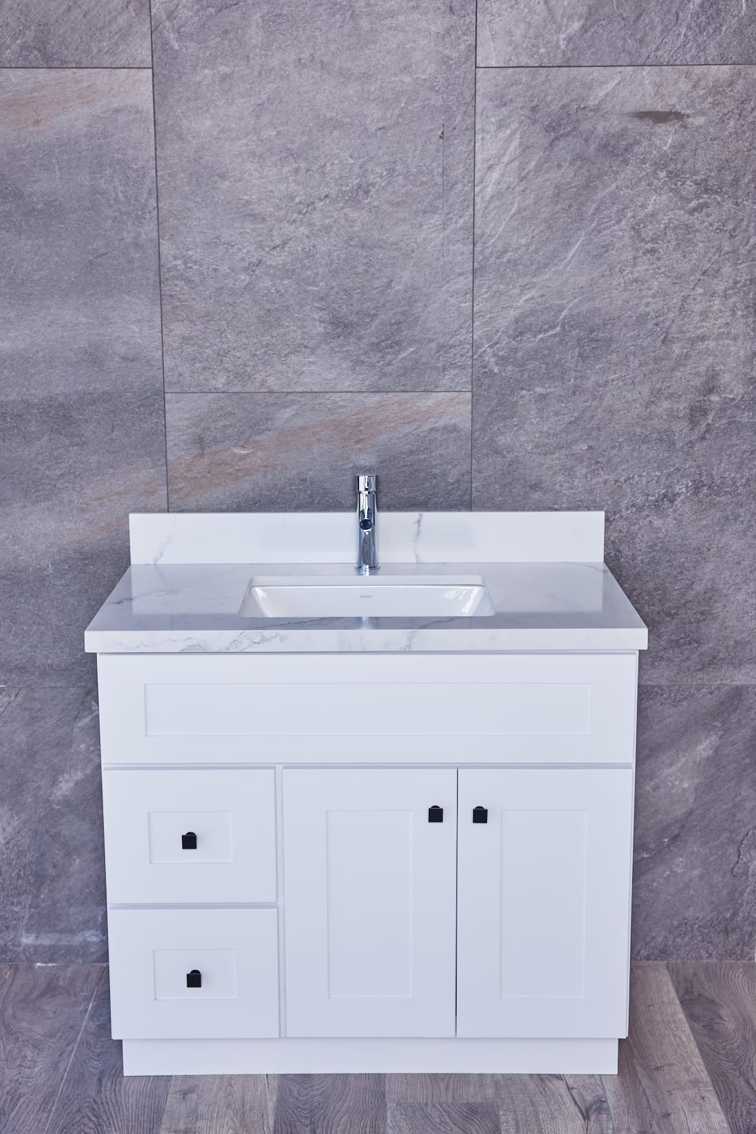 White bathroom vanity with marble countertop and modern faucet against gray tiled wall.